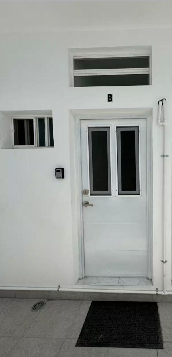 A white door with a small window above it, a black mat at the entrance, and a wall-mounted intercom. - Mini loft (Matamoros)