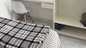 Une chambre à coucher comprenant un lit, un bureau, une chaise, un téléviseur et une étagère avec une boîte de mouchoirs.