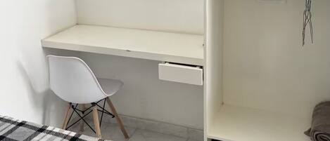 A bedroom with a bed, a desk, a chair, a TV, and a shelf with a box of tissues.