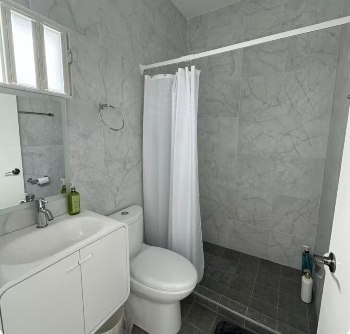A bathroom with a white toilet, a sink with a mirror, and a shower area with a curtain.