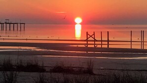 A beach scene with a sunset, a pier, and a fence.