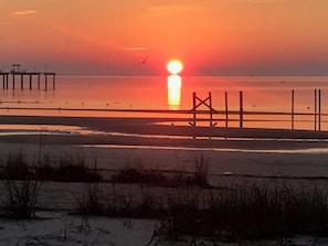 Une scène de plage avec un coucher de soleil, une jetée et une clôture.