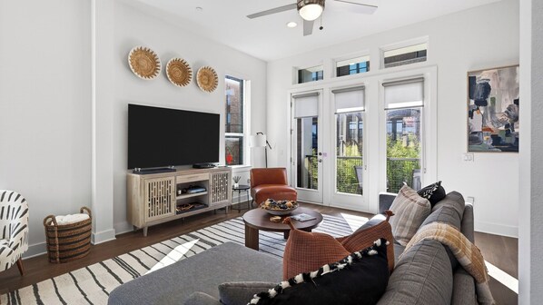 A living room with a television, sofa, armchair, and a large window with a view. - Rooftop Living in Central Austin Near UT, Dining & Music Concordia Retreat by Avantstay (Austin)