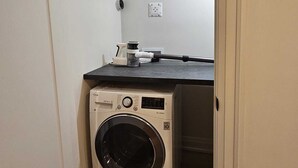 Une petite buanderie équipée d’un lave-linge, d’une machine à café et d’une prise électrique au mur.