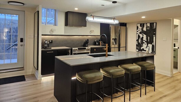 Une cuisine moderne dotée d’un îlot central, de tabourets de bar, d’un réfrigérateur en acier inoxydable et d’un grand tableau abstrait accroché au mur.