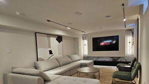 Un salon moderne avec un canapé d’angle, une table basse ronde, un téléviseur fixé au mur et une cheminée.