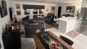 Un salon moderne comprenant un canapé, une table à manger avec des chaises et un coin cuisine avec un réfrigérateur et des placards.