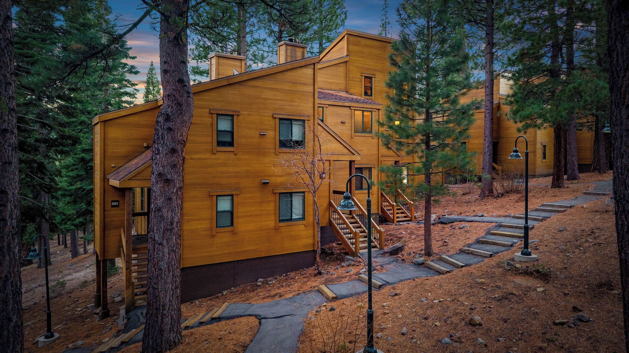 A wooden cabin with a staircase leading to the entrance, surrounded by pine trees.