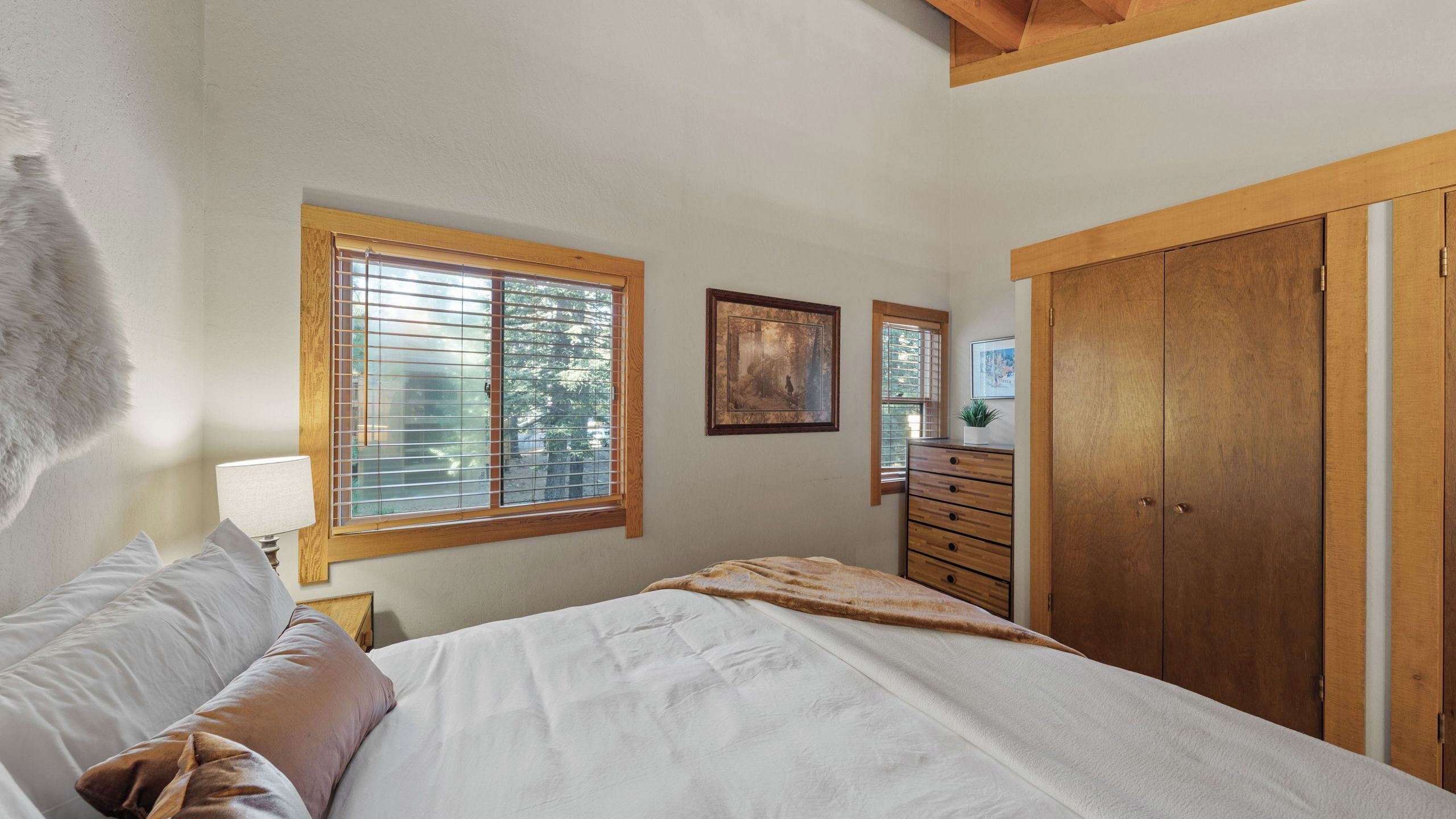 Une chambre à coucher comprenant un lit, une commode, une fenêtre avec des stores et une armoire.