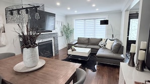 A modern living room with a wooden dining table, grey sofas, and a fireplace. - Beautiful Home with Hot Tub by Airport & 20 min to Downtown Toronto (Toronto)