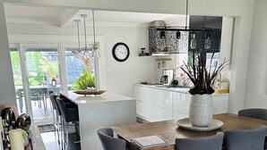 A modern kitchen with white cabinets, a dining area with a wooden table and grey chairs, and a view of the outdoors through large windows. - Beautiful Home with Hot Tub by Airport & 20 min to Downtown Toronto (Toronto)