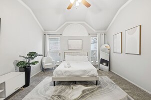 Un dormitorio moderno con una cama grande, una mesita de noche, una silla, una planta en maceta y obras de arte en las paredes.