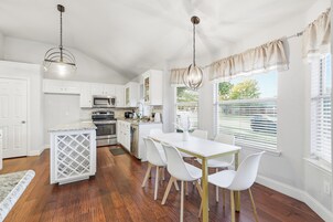 Una cocina moderna con armarios blancos, una isla central y un comedor con sillas blancas.