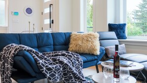Ett modernt vardagsrum med en blå soffa, ett runt soffbord och utsikt över grönområden utanför.