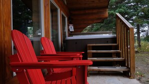 Una baita in legno con una vasca idromassaggio e poltrone Adirondack rosse all'esterno.