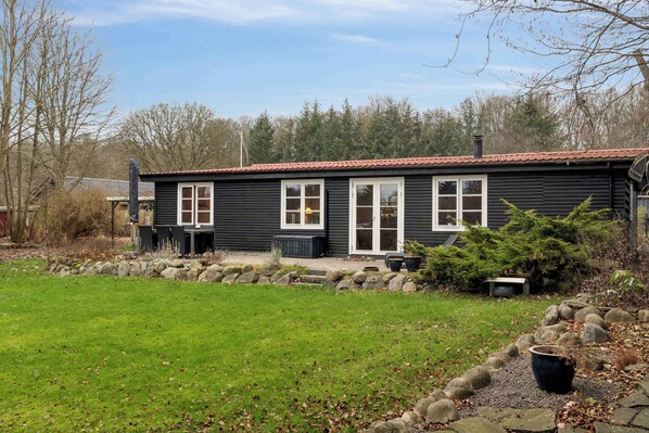 A black wooden cabin with a red-tiled roof, white-framed windows, and a stone pathway leading to the entrance.