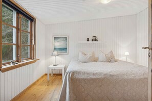 A bedroom with a bed, a nightstand, a lamp, a painting, and a window with blinds.