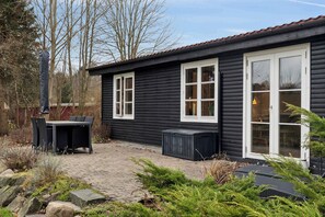 A black wooden house with white-framed windows and a patio area with a table and chairs.