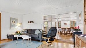 Un salon spacieux avec un canapé gris, un fauteuil en cuir noir, une table à manger avec des chaises et un buffet en bois.