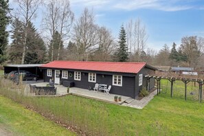 Ein Haus mit rotem Dach, einer Terrasse mit Gartenmöbeln und einem geparkten Auto davor.