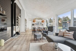 A modern living room with a sofa, ottoman, and a dining area with chairs and a table. - Lovely holiday home near Hals in North Jutland (Hals)