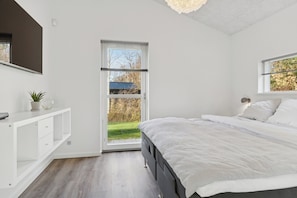 A bedroom with a large bed, a bedside table, a window, and a view of the outdoors. - Lovely holiday home near Hals in North Jutland (Hals)