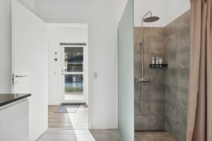A modern bathroom with a shower, a glass door leading to a balcony, and a small shelf with toiletries. - Lovely holiday home near Hals in North Jutland (Hals)