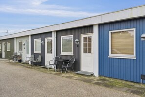 Een rij vakantiewoningen met aparte ingangen, elk voorzien van een klein terrasje en een tafel met stoelen.