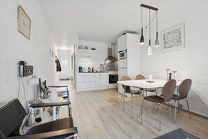 A modern kitchen with white cabinetry, a dining area with a white table and brown chairs, and pendant lighting. - Holiday home with views and peace by the fjord (Nørre Nebel)