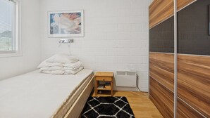 Une chambre à coucher avec un lit, une petite table de chevet en bois, un radiateur et un tableau encadré accroché au mur.