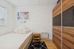 Ein Schlafzimmer mit einem Bett, einem kleinen Nachttisch, einem Heizkörper und einem gerahmten Bild an der Wand.