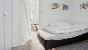 Ett sovrum med en säng, vita väggar och en dörr som leder till ett annat rum.
