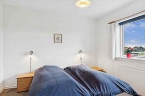 A bedroom with a bed, bedside lamps, a nightstand, a framed picture, and a window with a view.