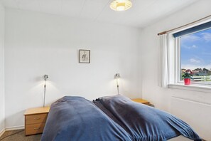 Un dormitorio con cama, mesitas de noche, ventana con vistas y una lámpara fijada a la pared.
