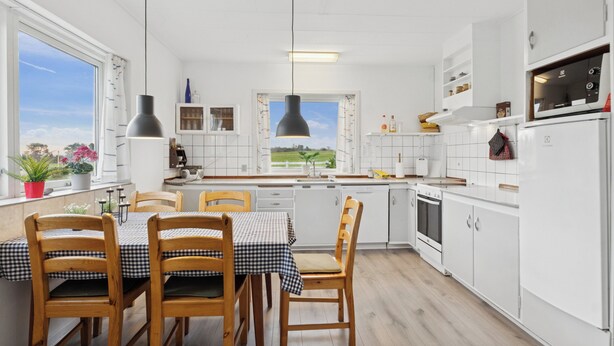 A modern kitchen with white cabinets, a dining table with checkered tablecloth, wooden chairs, and pendant lighting. - Holiday home on large grounds with beautiful view (Humble)