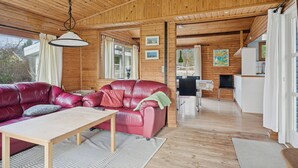 A wooden cabin interior with a red leather sofa, a dining table, and a kitchen area. - Cozy holiday home near the water (Dannemare)