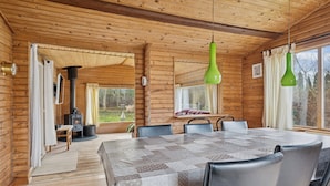 A wooden cabin interior with a dining table, chairs, a fireplace, and large windows. - Cozy holiday home near the water (Dannemare)