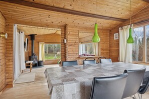 A wooden cabin interior with a dining table, chairs, a fireplace, and large windows. - Cozy holiday home near the water (Dannemare)