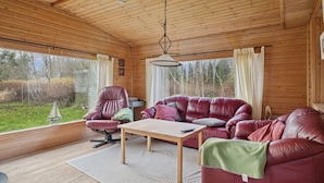 A wooden cabin interior with a leather sofa, a wooden table, and a hanging light fixture. - Cozy holiday home near the water (Dannemare)