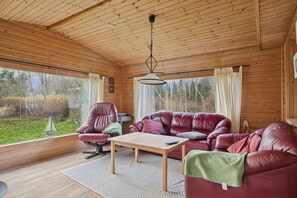 A wooden cabin interior with a leather sofa, a wooden table, and a hanging light fixture. - Cozy holiday home near the water (Dannemare)