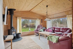 A cozy cabin interior with a wooden interior, a sofa, a table, and a fireplace. - Cozy holiday home near the water (Dannemare)