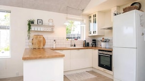 Eine moderne Küche mit weißen Schränken, einer Holzauskleidetheke, einem eingebauten Ofen und einem weißen Kühlschrank.