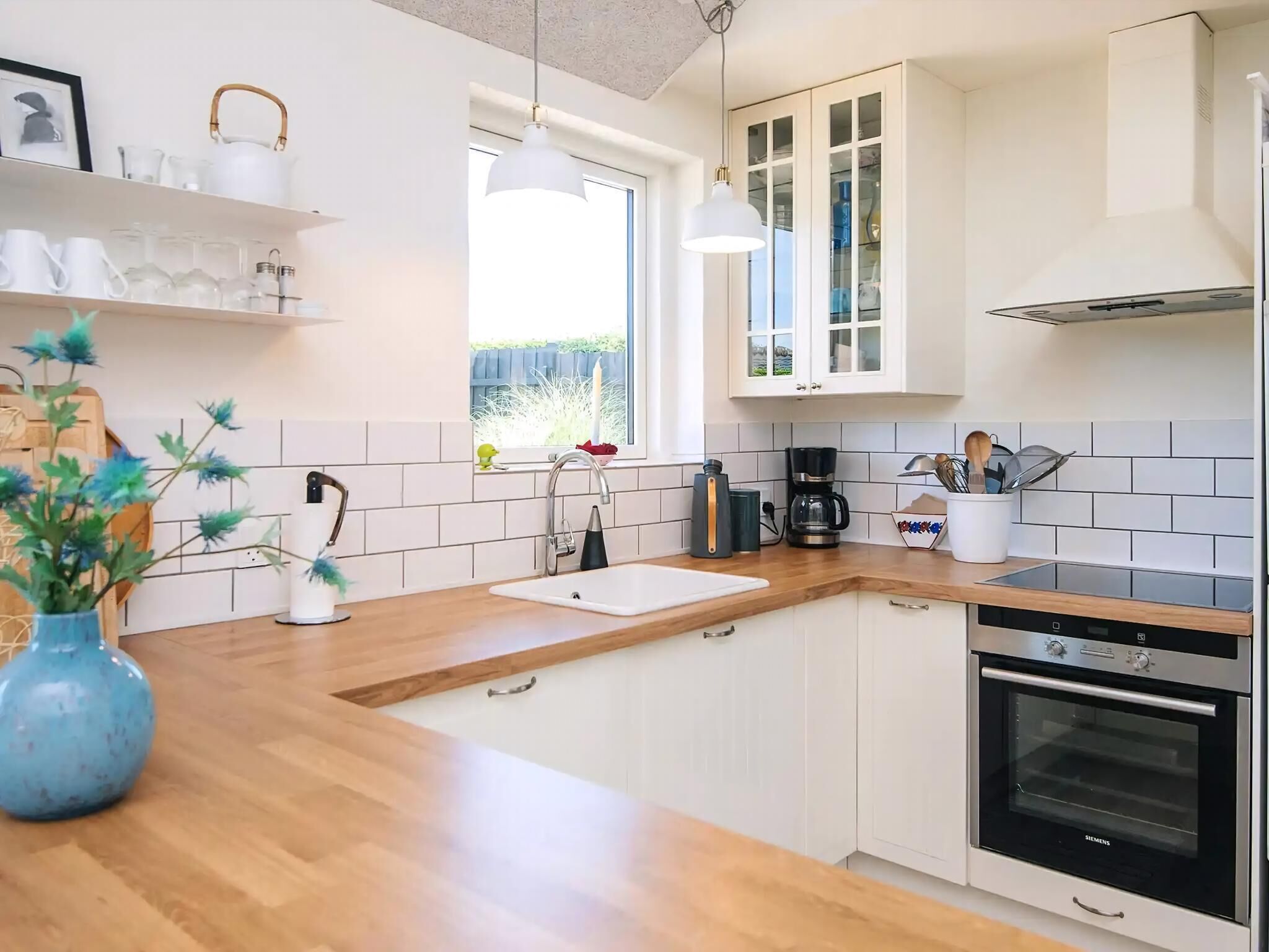 Una cocina moderna con armarios blancos, encimera de madera, horno Siemens y ventana con vistas a zonas verdes.