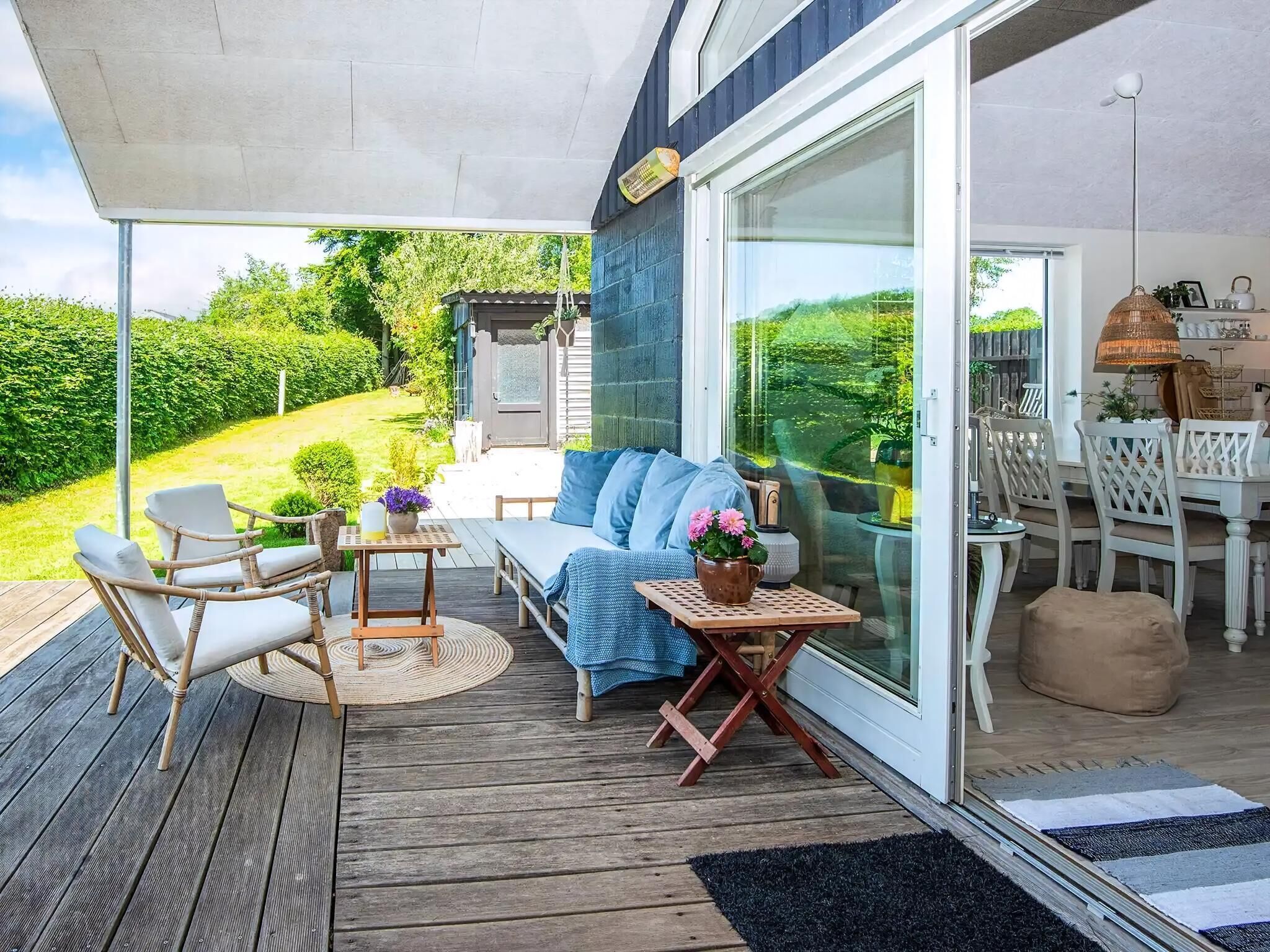 Een overdekt terras met een bank, stoelen en een tafel, met uitzicht op een tuin.