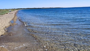 Ein Strand mit klarem Wasser, einem sandigen Ufer und einer entfernten Küstenlinie.