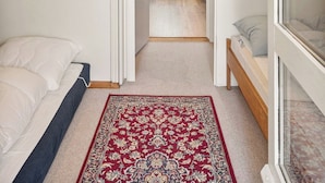 A bedroom with a sloped ceiling, a bed, a bedside table, a window, and a red patterned rug. - Idyllic summer house with sea view (Glesborg)