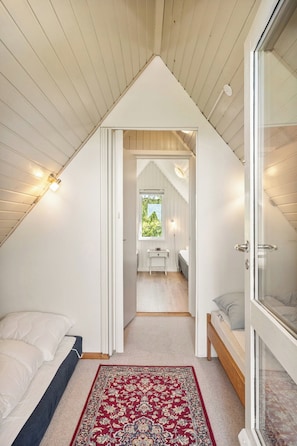 A bedroom with a sloped ceiling, a bed, a bedside table, a window, and a red patterned rug. - Idyllic summer house with sea view (Glesborg)