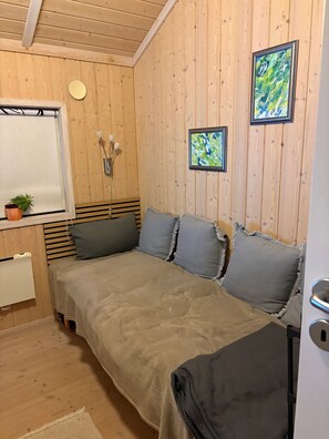 A wooden-paneled room with a bed, a small table with a plant, and two framed artworks on the wall. - Beautiful summer house from 2008 outdoor spa (Nakskov)
