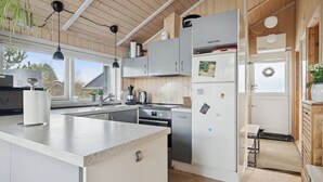 A modern kitchen with wooden beams, a large island, stainless steel appliances, and a view of the outdoors. - Beautiful summer house from 2008 outdoor spa (Nakskov)