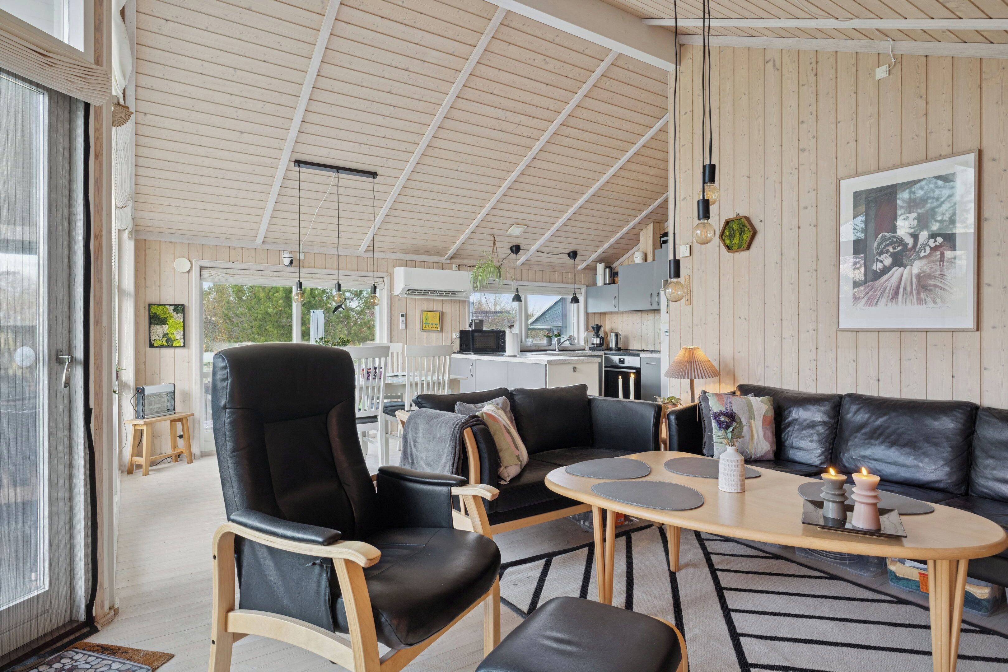 Et moderne interiør med træloft, en sort lædersofa, et spisebord og et køkkenområde.